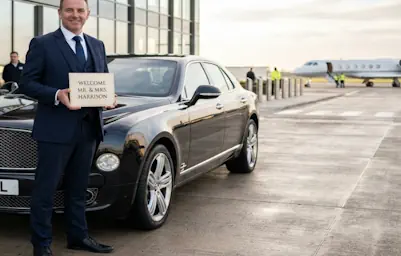 A driver waiting at the airport terminal for a client Bentley Mulsanne chauffeur service.